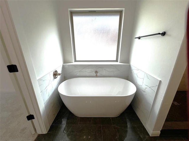 full bathroom featuring tile walls, a soaking tub, marble finish floor, and wainscoting