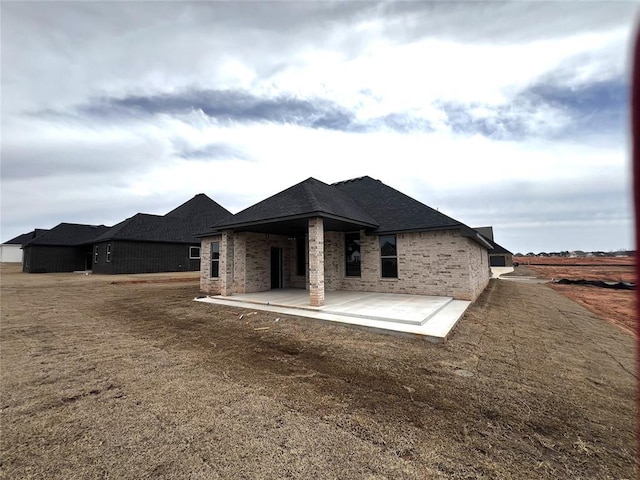 back of property with a patio area, brick siding, and roof with shingles