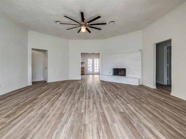 unfurnished living room featuring a ceiling fan, baseboards, a stone fireplace, light wood-style floors, and a textured ceiling