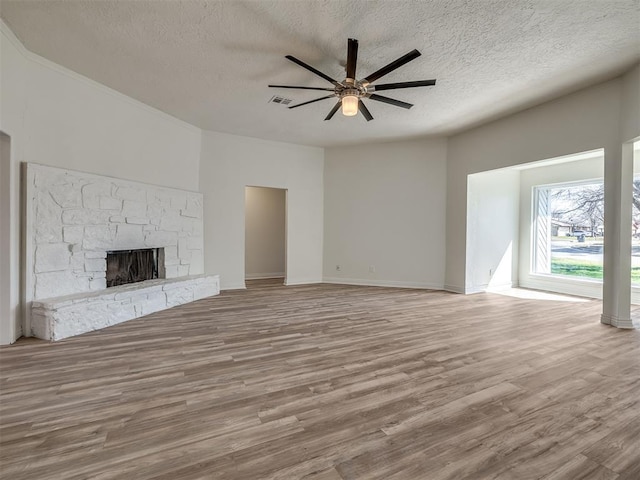 unfurnished living room featuring ceiling fan, a textured ceiling, a stone fireplace, and wood finished floors