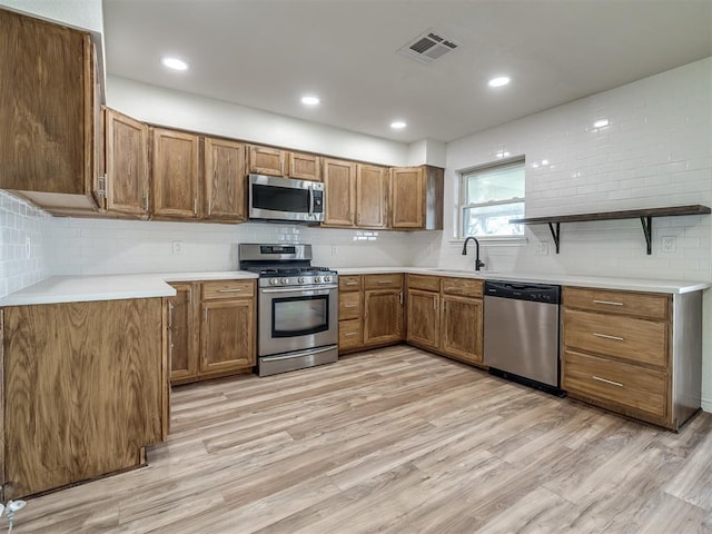 kitchen with visible vents, a sink, stainless steel appliances, light wood-style floors, and brown cabinets