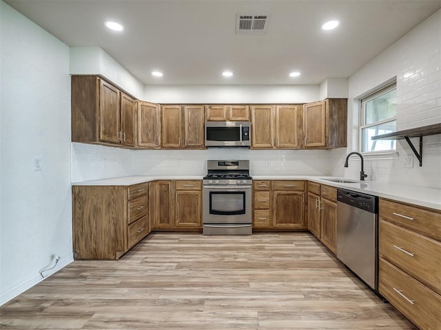 kitchen featuring visible vents, appliances with stainless steel finishes, light wood-style floors, brown cabinetry, and a sink