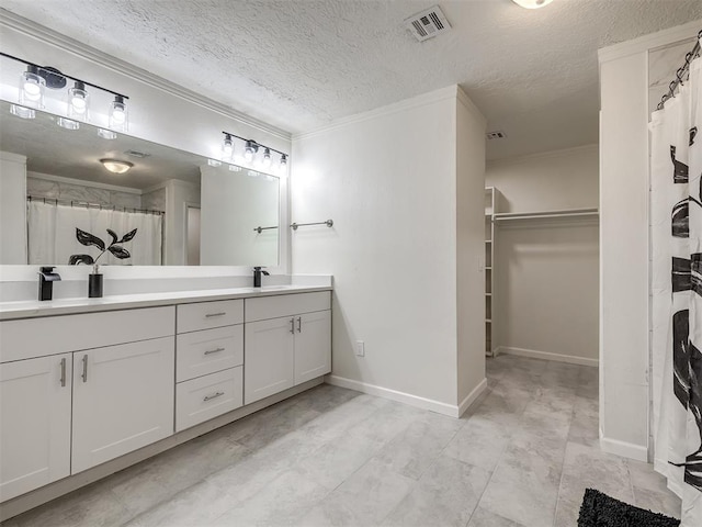 bathroom featuring visible vents, a walk in closet, crown molding, double vanity, and a sink