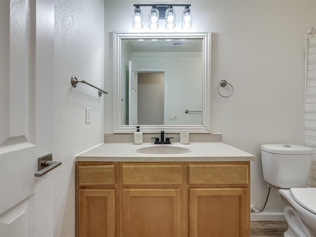 bathroom featuring vanity, toilet, and a textured wall