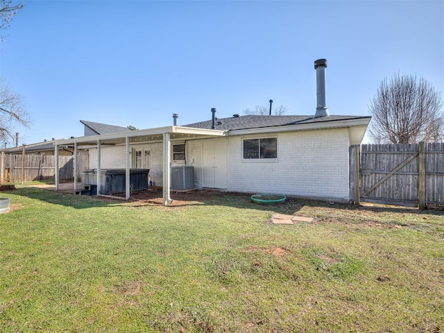 rear view of house with brick siding, a hot tub, central AC, a lawn, and a fenced backyard