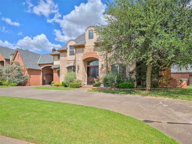 french provincial home with a front yard, brick siding, stone siding, and driveway