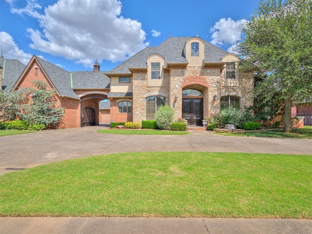 french country inspired facade featuring a front yard, stucco siding, a chimney, concrete driveway, and stone siding