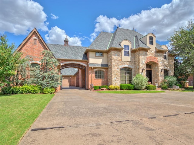 french provincial home with brick siding, a front yard, stucco siding, a chimney, and stone siding