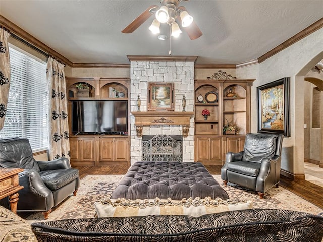 living area featuring wood finished floors, a ceiling fan, a fireplace, ornamental molding, and a textured ceiling