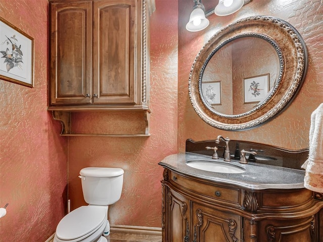 half bathroom with baseboards, toilet, vanity, and a textured wall