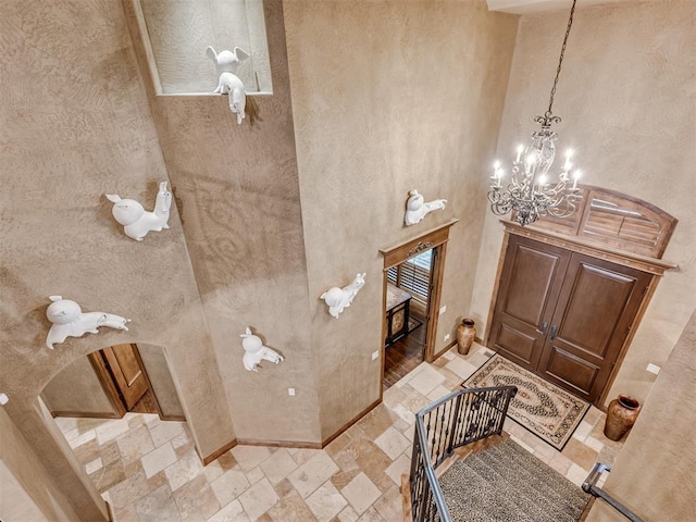 bathroom with stone tile floors, a notable chandelier, a high ceiling, and baseboards