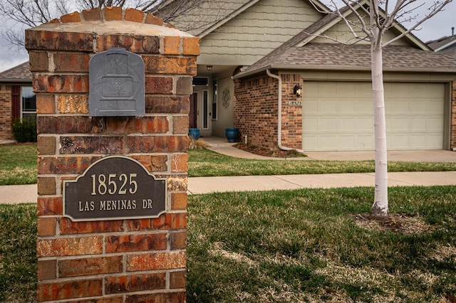 exterior space featuring a downspout, driveway, roof with shingles, gutters, and brick siding