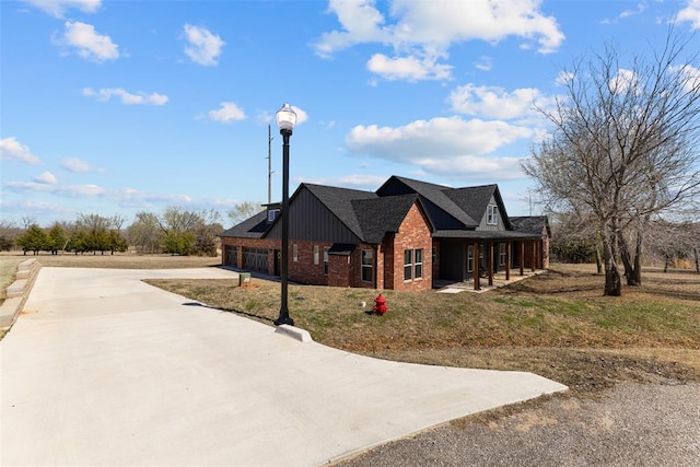 view of front of property featuring brick siding, board and batten siding, roof with shingles, covered porch, and driveway