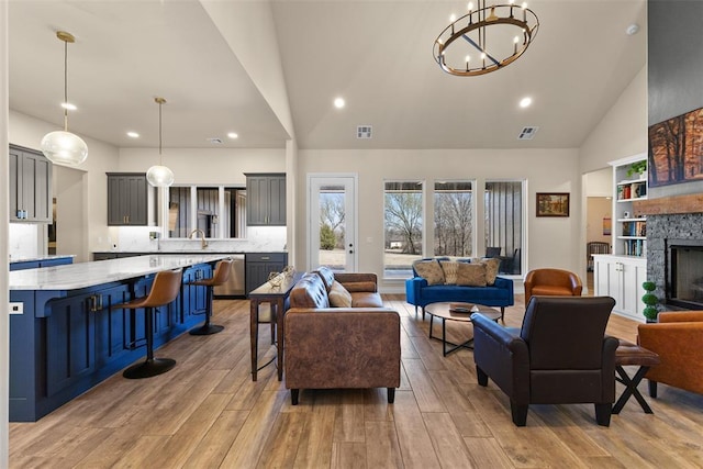 living room featuring a fireplace, light wood-style floors, visible vents, and a chandelier