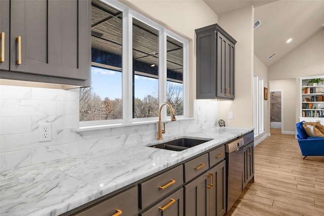 kitchen with tasteful backsplash, a sink, light stone countertops, light wood-style floors, and stainless steel dishwasher