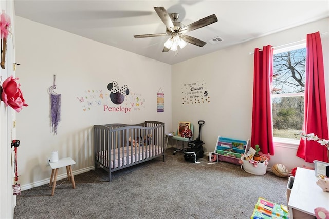 carpeted bedroom featuring baseboards, a crib, visible vents, and a ceiling fan