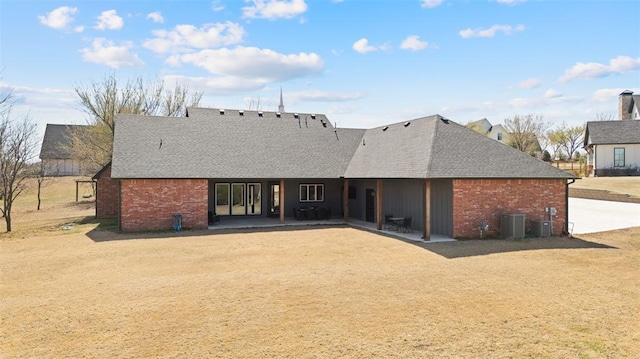 back of property with cooling unit, a patio area, brick siding, and roof with shingles