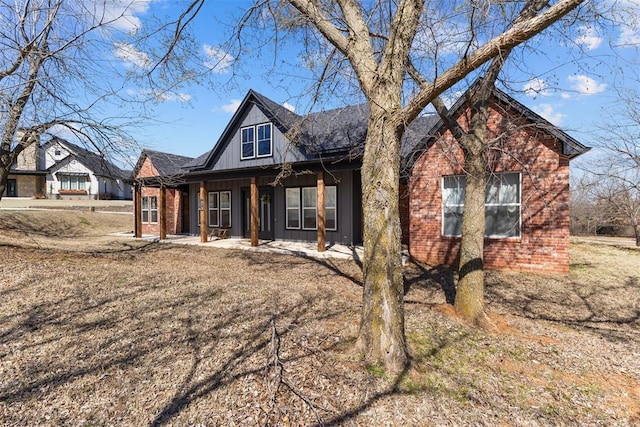 view of front of property featuring a porch, brick siding, board and batten siding, and a shingled roof