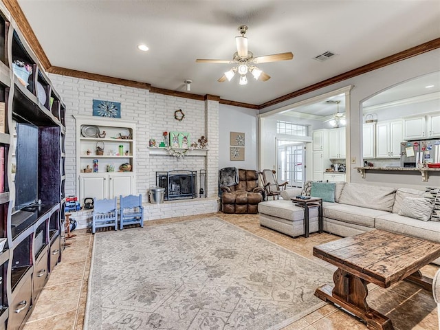 living area with visible vents, a brick fireplace, ceiling fan, and ornamental molding