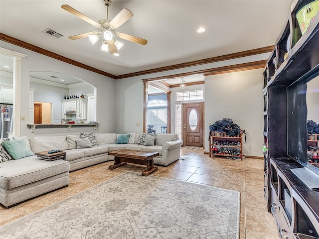 living room with visible vents, arched walkways, light tile patterned flooring, crown molding, and ceiling fan