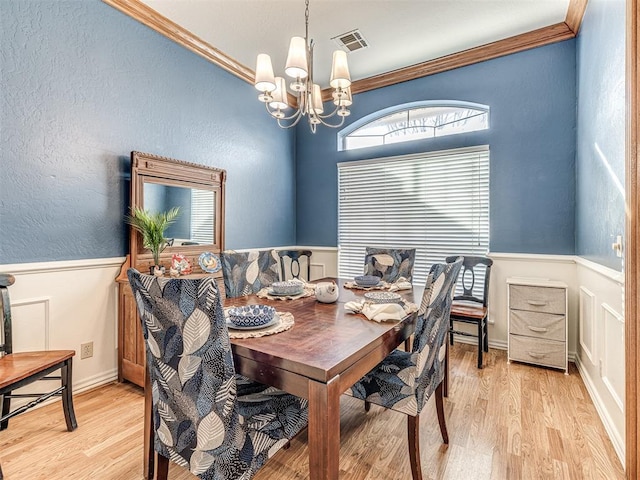 dining space featuring visible vents, ornamental molding, light wood-style flooring, wainscoting, and a notable chandelier