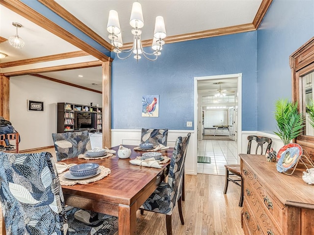 dining room featuring crown molding, light wood-style flooring, a wainscoted wall, and a chandelier