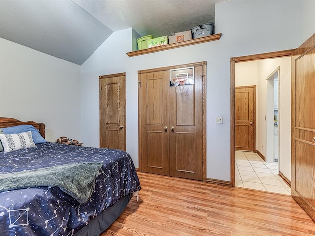 bedroom with light wood-style flooring, a textured ceiling, lofted ceiling, and multiple closets