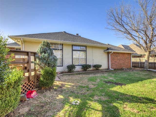 rear view of property with brick siding, a lawn, and fence