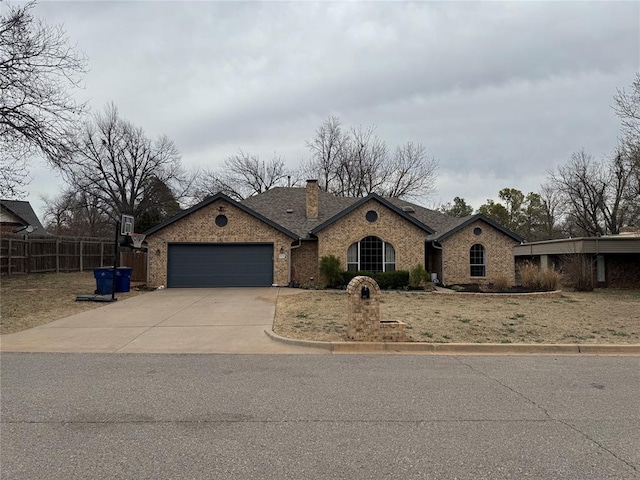 view of front facade with fence, driveway, an attached garage, a chimney, and brick siding