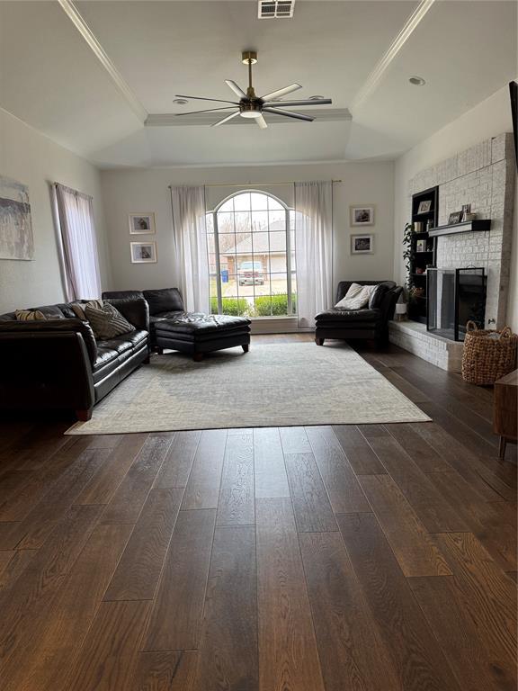 living room featuring dark wood-style floors, visible vents, a ceiling fan, a tray ceiling, and a fireplace