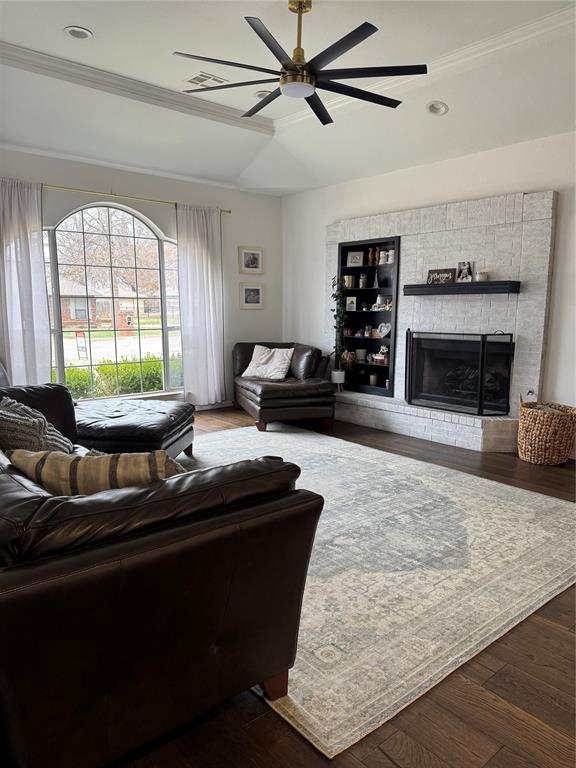 living area featuring ornamental molding, a ceiling fan, a tray ceiling, wood finished floors, and a fireplace