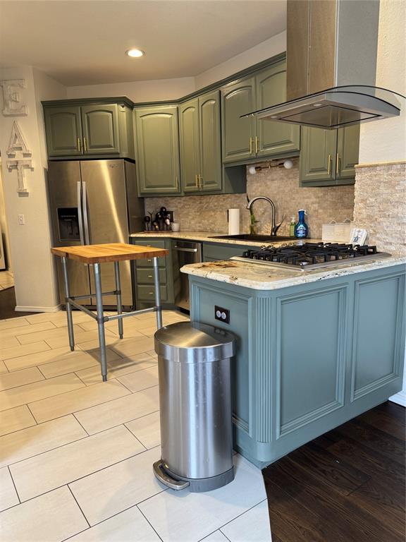 kitchen featuring a sink, tasteful backsplash, stainless steel appliances, a peninsula, and wall chimney range hood