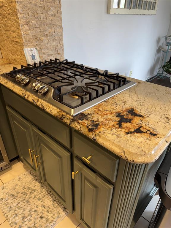 details with stainless steel gas stovetop, light stone countertops, and tasteful backsplash