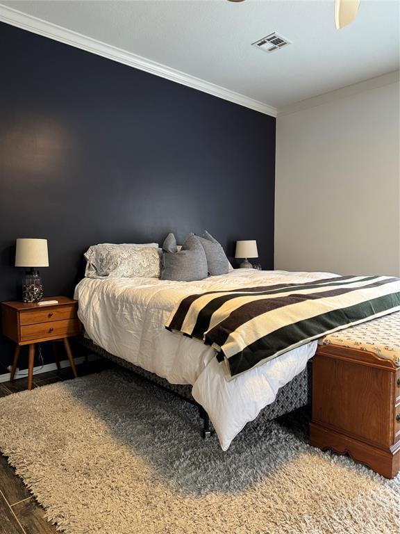 bedroom featuring visible vents, wood finished floors, and ornamental molding