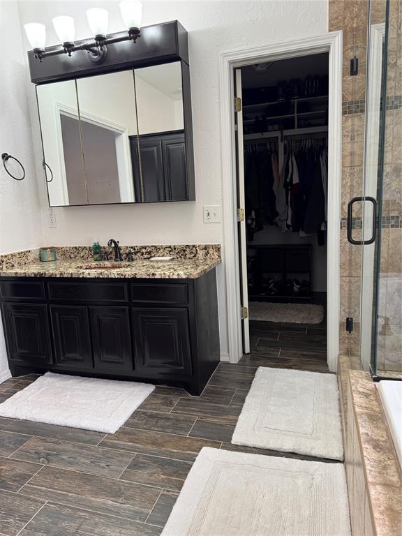 bathroom with a spacious closet, a shower stall, vanity, and wood tiled floor