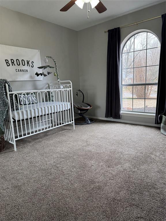 bedroom with baseboards, a crib, carpet, and ceiling fan