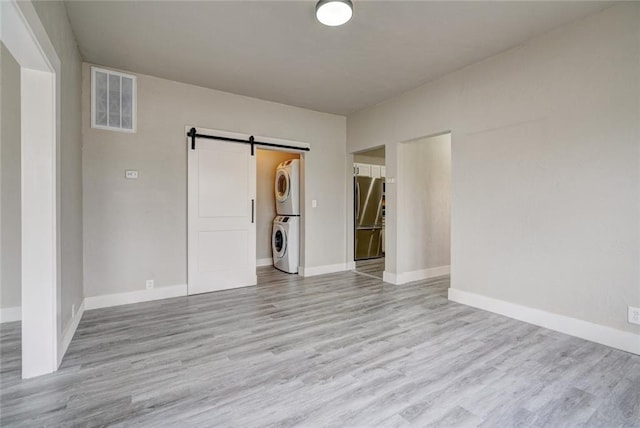 324 NW 24th St, Oklahoma City, OK 73103 - unfurnished room featuring visible vents, baseboards, a barn door, stacked washer and clothes dryer, and wood finished floors