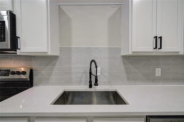 324 NW 24th St, Oklahoma City, OK 73103 - kitchen with light stone countertops, a sink, white cabinets, appliances with stainless steel finishes, and tasteful backsplash
