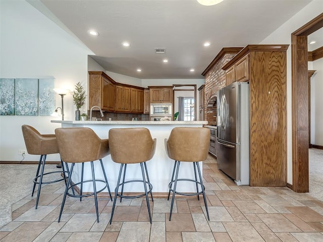 kitchen featuring visible vents, a breakfast bar, appliances with stainless steel finishes, a peninsula, and brown cabinetry