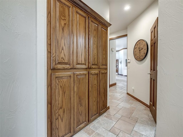 corridor with recessed lighting, a textured wall, baseboards, and stone tile flooring