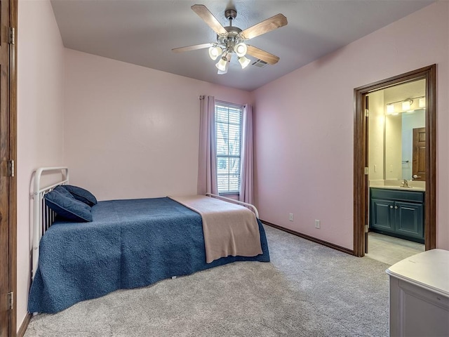 bedroom featuring baseboards, light colored carpet, ensuite bathroom, a ceiling fan, and a sink