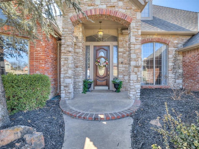 view of exterior entry featuring brick siding, stone siding, and a shingled roof