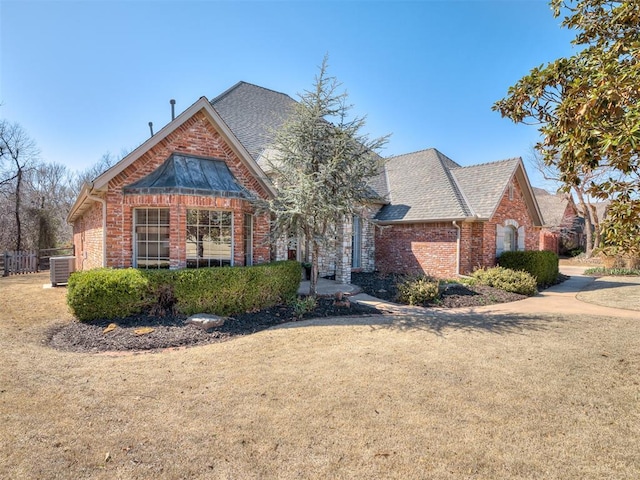 view of front of property featuring central air condition unit, brick siding, roof with shingles, and a front yard