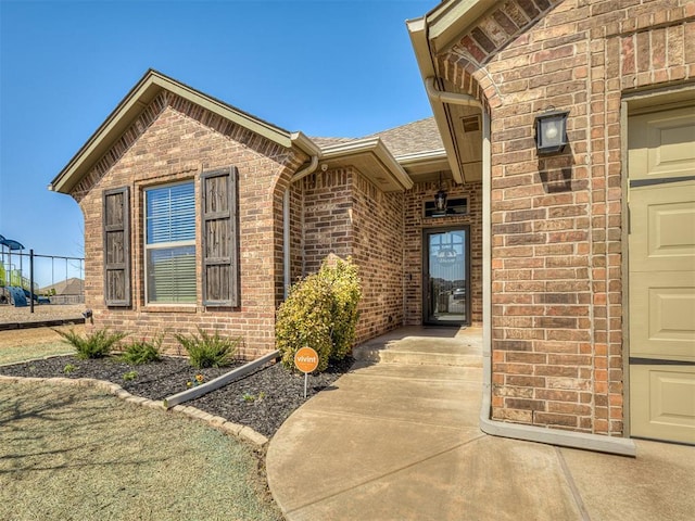 doorway to property featuring brick siding, an attached garage, and a shingled roof