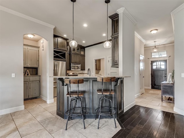 kitchen with a kitchen bar, stainless steel appliances, dark brown cabinetry, crown molding, and light stone countertops