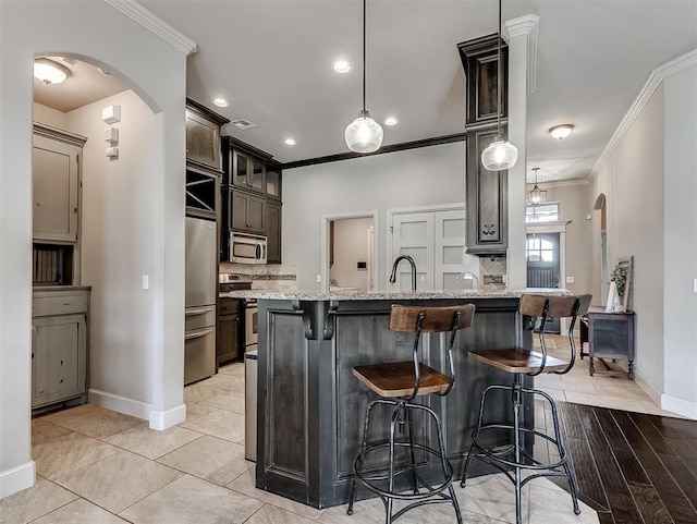 kitchen with stainless steel appliances, arched walkways, a breakfast bar, and ornamental molding