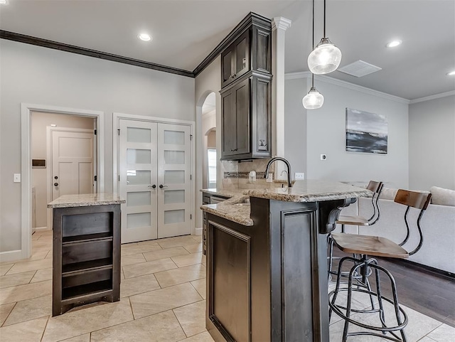 kitchen with light stone counters, a kitchen breakfast bar, arched walkways, crown molding, and dark brown cabinets