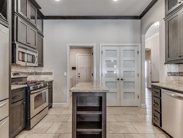 kitchen featuring light stone counters, light tile patterned floors, arched walkways, ornamental molding, and stainless steel appliances