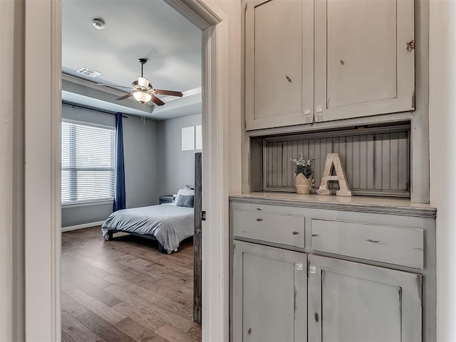 bedroom with wood finished floors, baseboards, visible vents, ceiling fan, and a raised ceiling