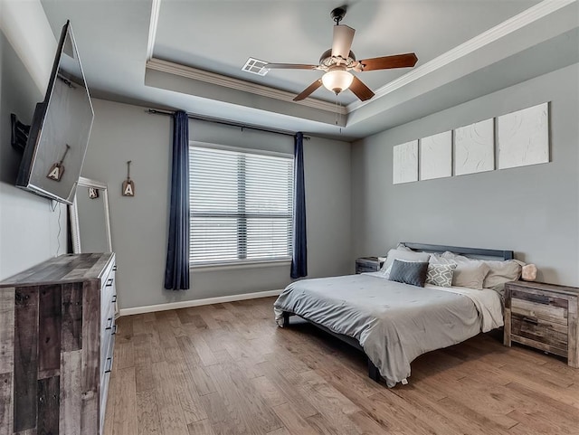 bedroom featuring visible vents, baseboards, a tray ceiling, ornamental molding, and light wood-style flooring